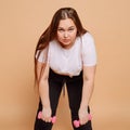 Exhausted overweight girl with dumbbells on beige background