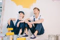 Painters in overalls sitting on floor near wall