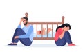Exhausted parents at the crib with crying baby. Sad woman sitting on the floor, crying and hugging her knees. Tired father with Royalty Free Stock Photo