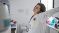 Exhausted yet resolute, young hispanic scientist woman stretching arms at computer in lab, amidst research analysis Royalty Free Stock Photo