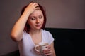 Exhausted or sick woman sitting on sofa with cup of coffee holding hand on forehead. A little break concept