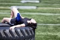 Exhausted teen girl resting on heavy truck tire in middle of sports field during hot day