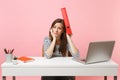 Exhausted woman holding red folder with paper document near head working on project while sit at office with laptop Royalty Free Stock Photo