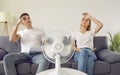 Exhausted woman and man sitting in front of electric fan sweating through great summer heat.