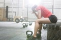 Exhausted woman sitting on tire in crossfit gym