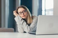 Exhausted woman at work yawns from painful sensations caused by wrong posture, sedentary work, long sitting at a laptop Royalty Free Stock Photo