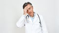 Exhausted and worried mature doctor in medical uniform with stethoscope around neck touching forehead with hand while Royalty Free Stock Photo