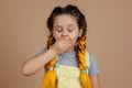 Exhausted yawning little girl with yellow kanekalon pigtails, with closed eyes closing mouth with hand in yellow