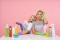 Exhausted young attractive blonde cleaning ladies wearing working clothes and rubber gloves while sitting over pink background,