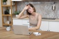 Young attractive woman sitting at the table and working on laptop in the kitchen at home Royalty Free Stock Photo