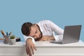 Exhausted young businessman sleeping on his desk, tired of overworking on blue studio background, copy space Royalty Free Stock Photo