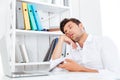 Exhausted young businessman sleeping while sitting at the office desk