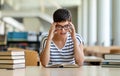 Exhausted young female studying and preparing for exam in college library. Education people concept