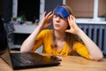 Exhausted young woman raises slightly her eye mask, trying to open sleepy eyes, needs more rest after hard work at laptop, out of Royalty Free Stock Photo