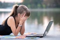 Exhausted young woman working behind laptop computer lying down in summer park outdoors. Problems with remote work concept Royalty Free Stock Photo