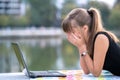 Exhausted young woman working behind laptop computer lying down in summer park outdoors. Problems with remote work concept Royalty Free Stock Photo