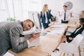 exhausted zombie like businessman sleeping on copier while his colleagues having conversation