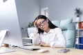 Exhaustion at work. A young Asian woman in glasses holds her head, feels pain, grimaces. Royalty Free Stock Photo