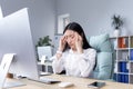 Exhaustion at work. A young Asian woman holds her head, feels pain, grimaces. Royalty Free Stock Photo