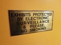 Exhibits protected by electronic surveillance and please no smoking sign on yellow wall