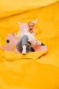 Exhilarated young woman tearing a hole through big sheet of cramped yellow paper