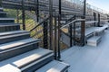 Exit, entrance, vomitorium at empty metal stadium bleacher seats along aisle with steps and railing.