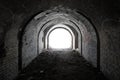 Exit from the old dark brick arched tunnel of the 19th century fortification. Light in the end of old abandoned tunnel Royalty Free Stock Photo