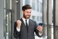 Exited Businessman Celebrating Achievement looking at Smartphone outdoor. Successful business man celebrating win with mobile
