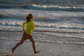 Exited carefree little boy running on wet coast near waving sea on sunny summer day. Kid running at summer beach Royalty Free Stock Photo