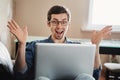 Exited young man in glasses is reading good news on laptop