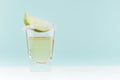 Exotic coctail with sour green lime in shot glass with sugar rim on soft light mint color background and white wood board.