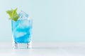 Exotic cold shot glass cocktail with blue curacao, ice cubes, green mint on soft light mint color background and white wood board. Royalty Free Stock Photo