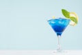 Exotic cold shot glass cocktail with blue curacao, ice cubes, lemon slice, yellow straw, green mint on soft light mint color. Royalty Free Stock Photo