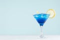 Exotic cold shot glass cocktail with blue curacao, ice cubes, lemon slice, yellow straw on soft light mint color background. Royalty Free Stock Photo