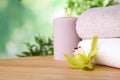 Exotic flower, burning candle and fresh towels on table against blurred green background, space for text