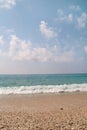 Exotic sandy beach, tropical mediterranean sea with waves and sea foam, blue sky and clouds. Natural environment, landscape. Royalty Free Stock Photo