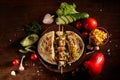 Exotic still slife with pita, fresh vegetables and kebab over wooden background, selective focus.