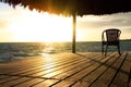 Exotic wooden gazebo and chair on the beach at sunset or sunrise. Background of a seashore with seat, resting pavilion, palm trees Royalty Free Stock Photo