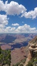 Expansive blue skies with fluffy clouds hover above the Grand Canyon's layered geological history, offering a