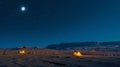 An expansive desert landscape bathed in moonlight with a secluded campsite tucked a the dunes its tents glowing