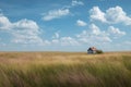 Expansive field of grass with a quaint house in the distance under a blue sky dotted with clouds Royalty Free Stock Photo