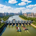 Expansive river dam with barges and modern city skyline under a bright blue sky with fluffy clouds Royalty Free Stock Photo
