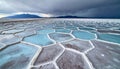 Hexagonal Salt Flats with Blue Water Pools and Mountains Under Stormy Sky Royalty Free Stock Photo