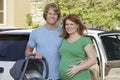 Expectant Couple With Cradle Standing By Car