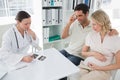 Expectant couple and doctor discussing over reports Royalty Free Stock Photo