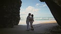 Expectant father mother kissing standing sand beach in stone cliff shadow. Royalty Free Stock Photo