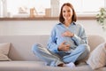 expectant lady awaiting baby sitting on sofa touching belly indoor Royalty Free Stock Photo