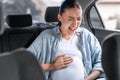 Expectant mother feels sudden abdominal cramps, touching tummy in automobile