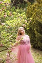 Expectant mother in gently pink negligee stands near the magnolia which blooms with pink flowers.