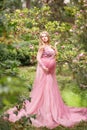 Expectant mother in beautiful long dress in garden near blooming magnolia
